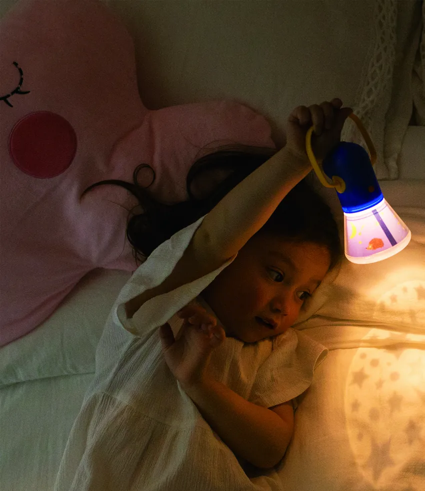 A child under a blanket reading with a mideer storybook torch